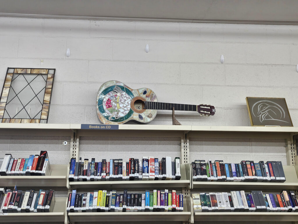 Art pieces in the library including a stained-glass cabinet door, a guitar with glass designs and a woman huddled over etched on a mirror.